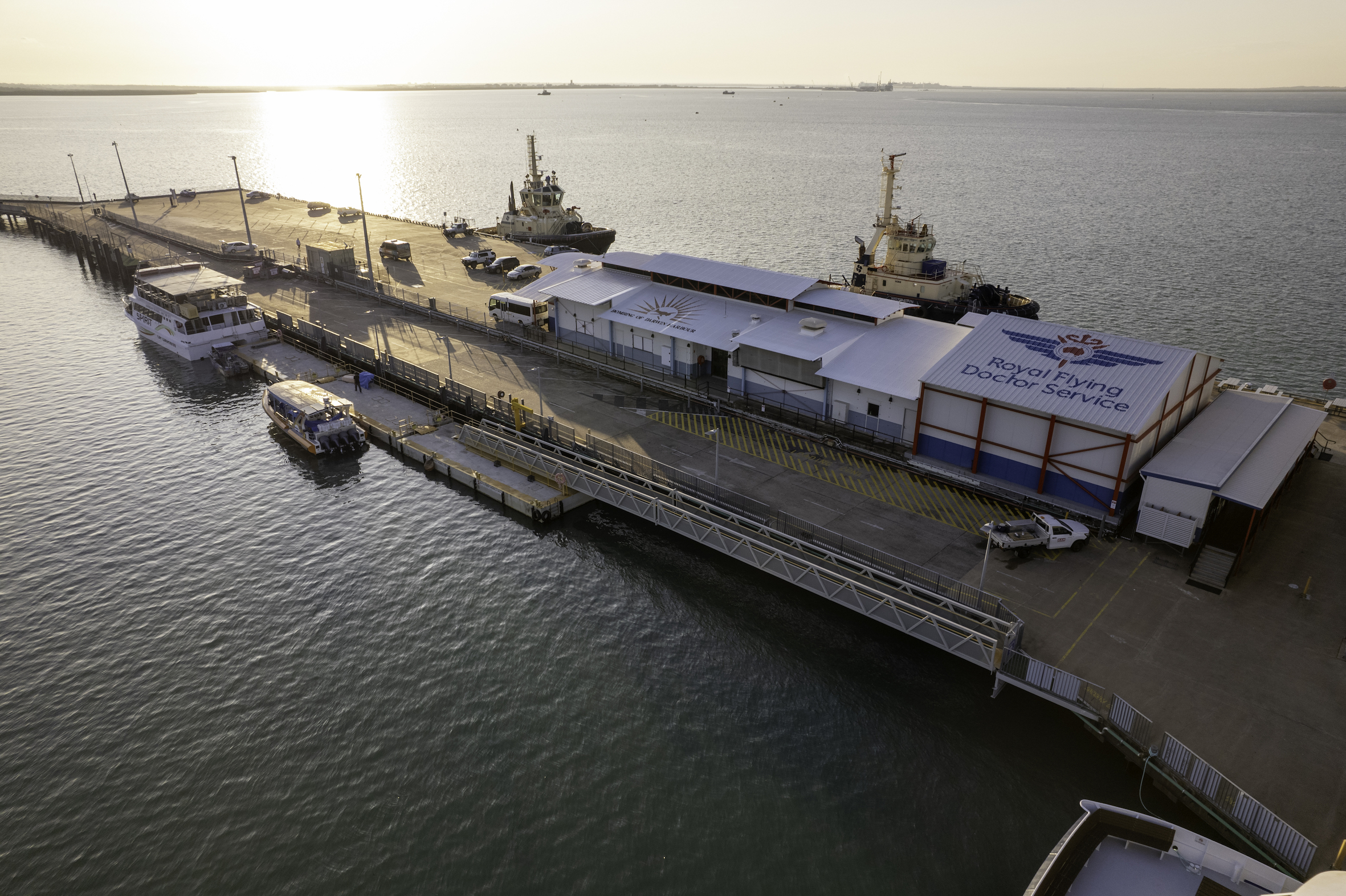 Stunning aerial view of Darwin dock with boats, RFDS Aviation Attraction Ticket building, and vibrant sunset reflecting on the waterfront.