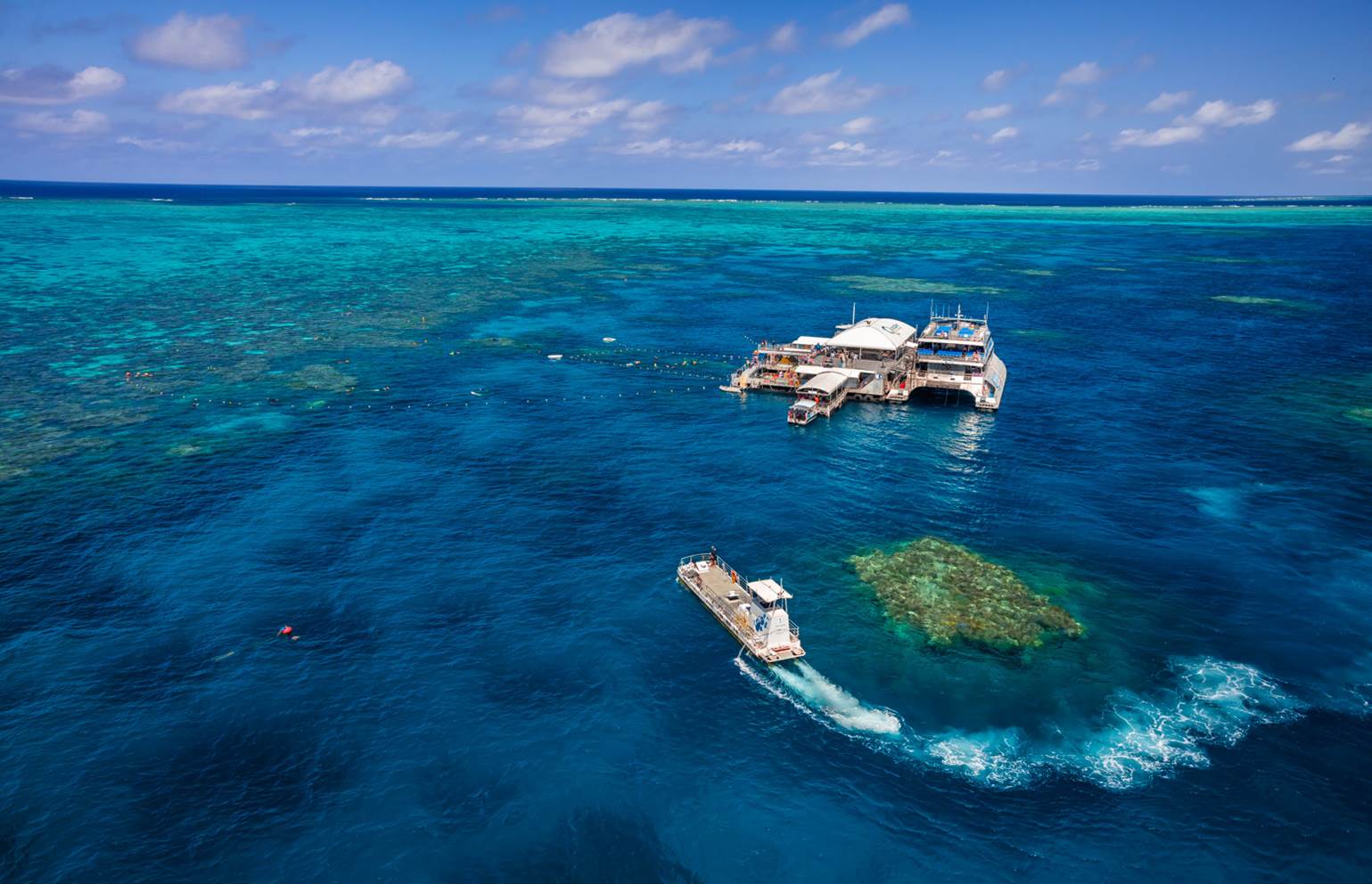 Experience a boat arriving at the Quicksilver Outer Barrier Reef Platform atop crystal-clear blue waters and colourful tropical coral reefs.