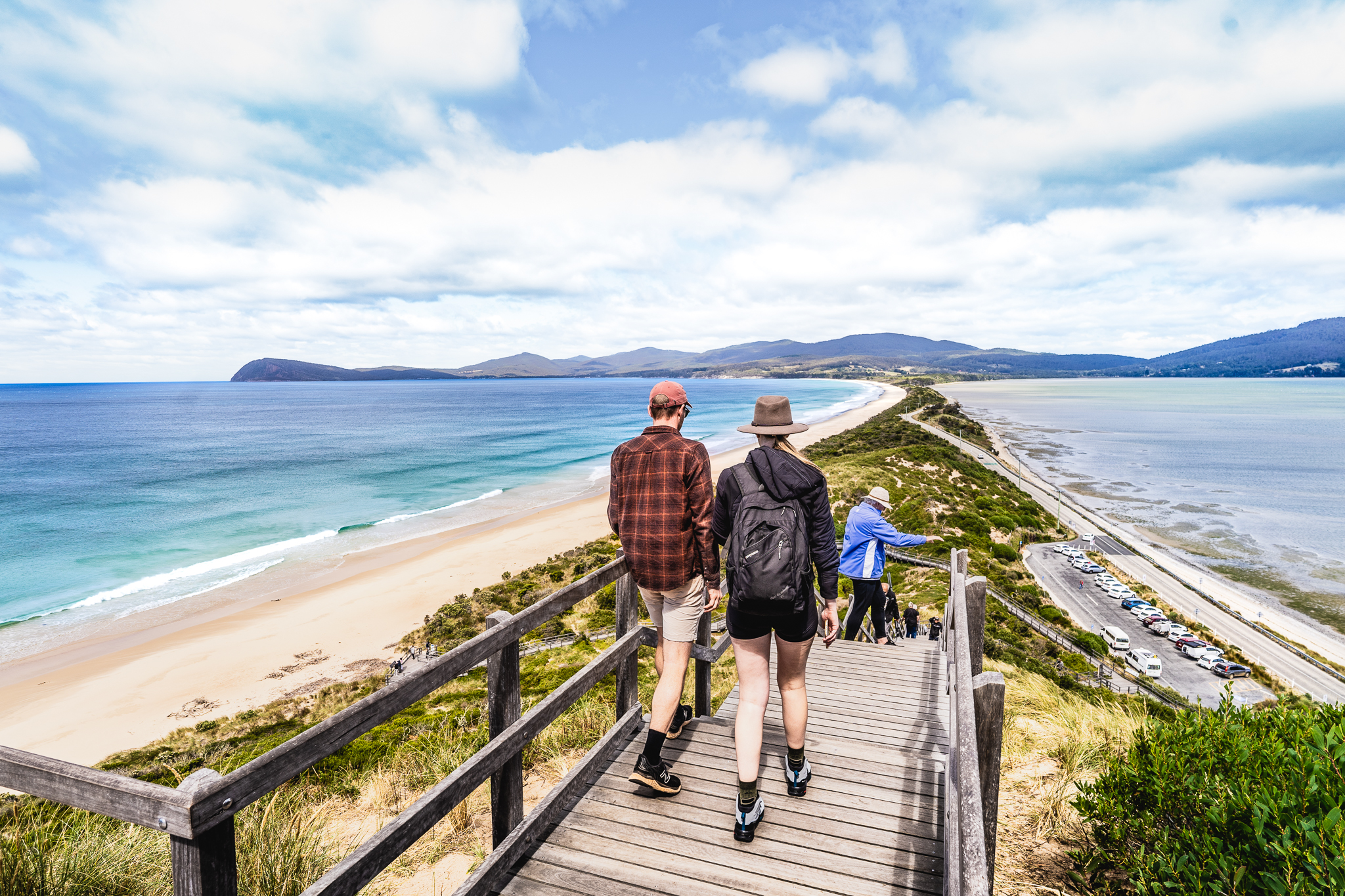 Visitors descend a wooden staircase overlooking the picturesque Bruny Island beach on a scenic food, sightseeing, and lighthouse tour.