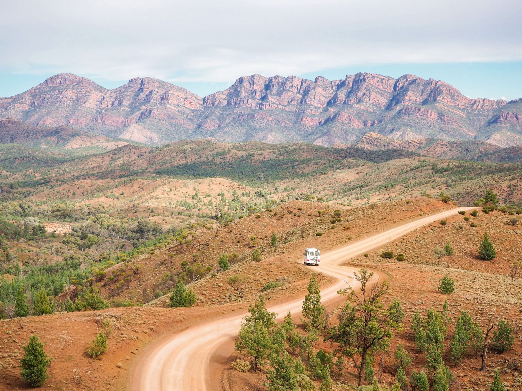 Scenic dirt road with white caravan on 6-Day Eyre Peninsula Flinders Ranges Adventure Tour headed towards dramatic rocky mountain ranges.