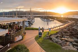 Vibrant sunset over marina with moored sailboats, people walking, and Sundowner Cruise & Dine at Sorrentos Restaurant visible on left.