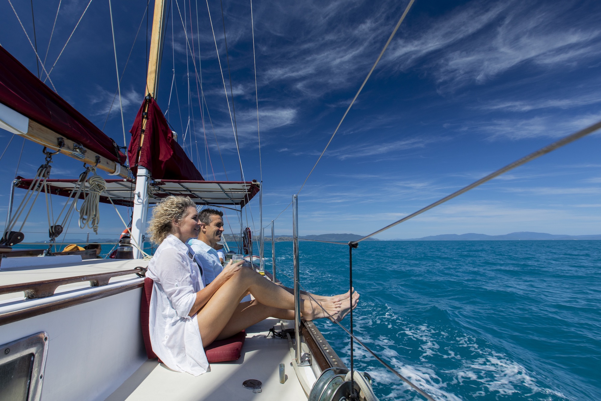 Two people unwind on Lady Enid yacht under sunny skies, overlooking turquoise waters near Whitehaven Beach after a snorkelling adventure.