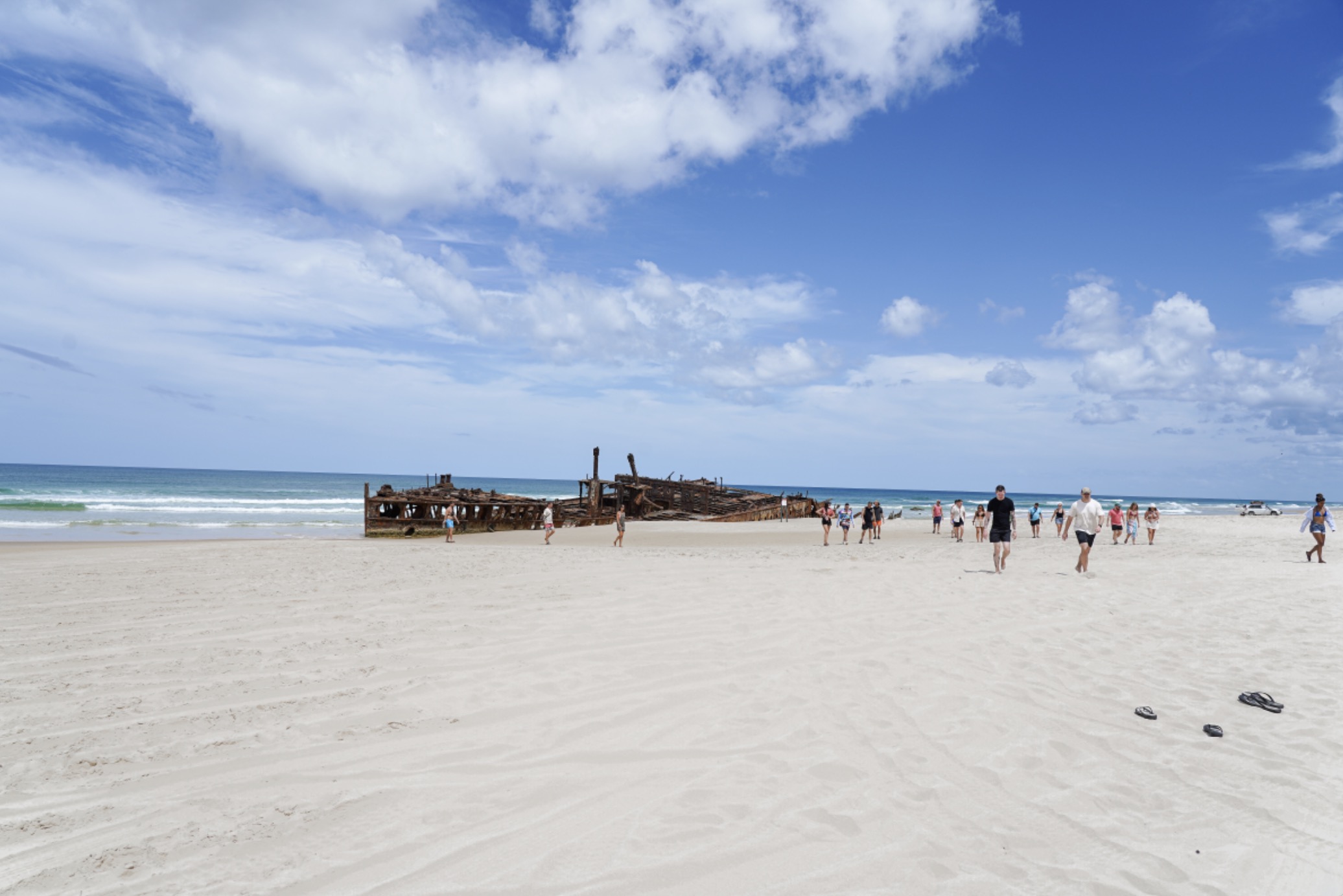 Visitors explore a scenic sandy beach, approaching a famous shipwreck on Fraser Island during the top-rated K'gari Safari 4WD tour.