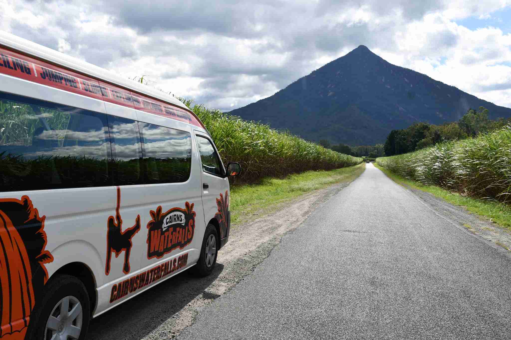 Explorer Tour van parked on a scenic rural road, surrounded by lush grassy fields and a majestic mountain in the background.