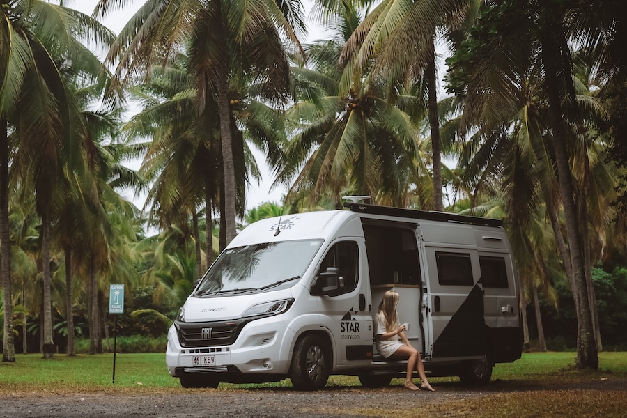 a girl sitting in the back of a campervan in a rainforest in cairns